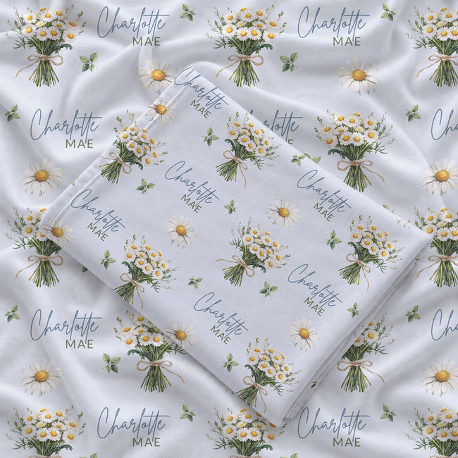 Personalized pale blue swaddle blanket with white daisy bouquets, scattered flowers, green leaves, and the name Charlotte Mae.