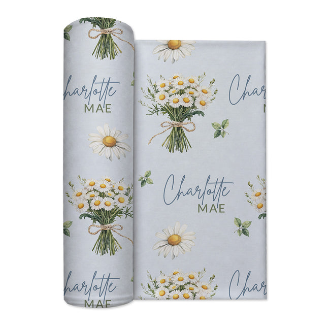Personalized pale blue swaddle blanket with white daisy bouquets, scattered flowers, green leaves, and the name Charlotte Mae.