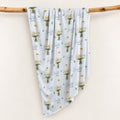 Personalized pale blue swaddle blanket with white daisy bouquets, scattered flowers, green leaves, and the name Charlotte Mae.
