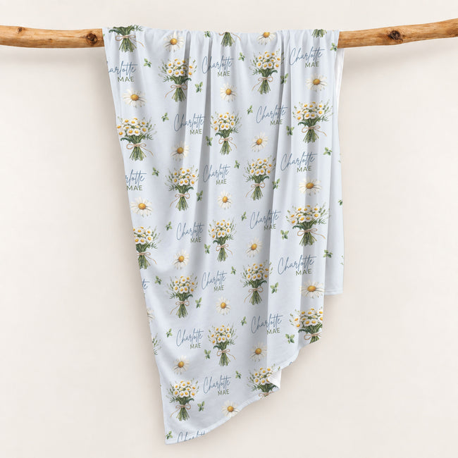Personalized pale blue swaddle blanket with white daisy bouquets, scattered flowers, green leaves, and the name Charlotte Mae.