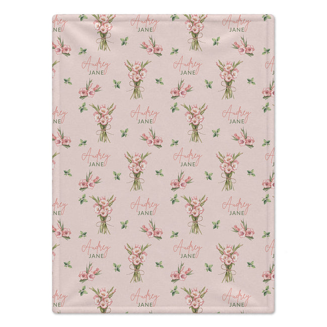 Blush pink blanket with pink gladiolus bouquets, green leaves, and the name Audrey Jane in coral script and green lettering.