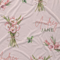 Blush pink fabric with pink gladiolus bouquets, green leaves, and the name Audrey Jane in coral script and green lettering.