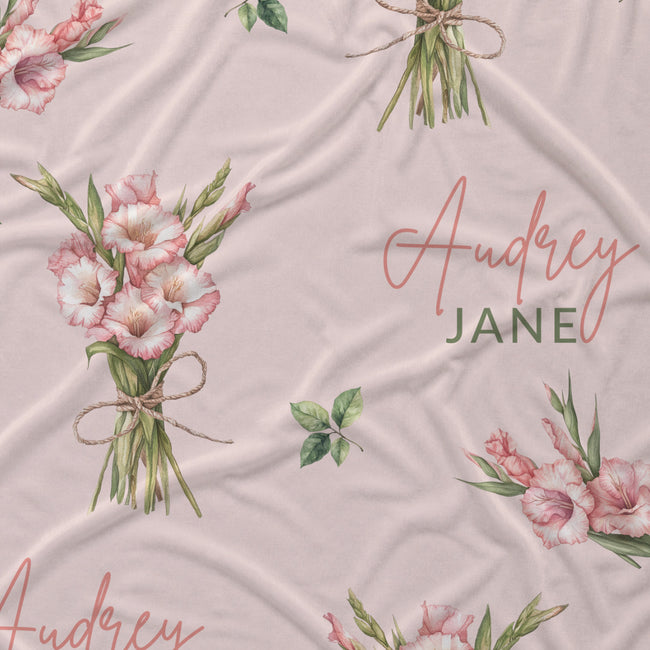 Blush pink fabric with pink gladiolus bouquets, green leaves, and the name Audrey Jane in coral script and green lettering.