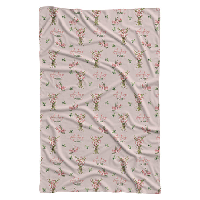 Blush pink swaddle blanket with pink gladiolus bouquets, scattered green leaves, and the name Audrey Jane repeated throughout.
