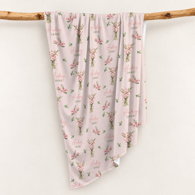 Blush pink swaddle blanket with pink gladiolus bouquets, scattered green leaves, and the name Audrey Jane repeated throughout.