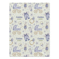 A personalized baby blanket with a watercolor pattern of baby strollers, outfits, pacifiers, and rings on a cream background, featuring the custom name 'Caiden James' printed twice.