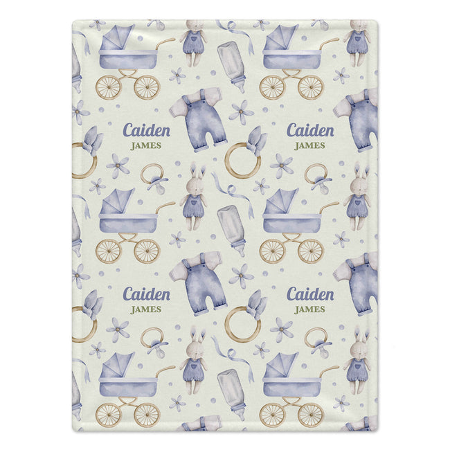 A personalized baby blanket with a watercolor pattern of baby strollers, outfits, pacifiers, and rings on a cream background, featuring the custom name 'Caiden James' printed twice.