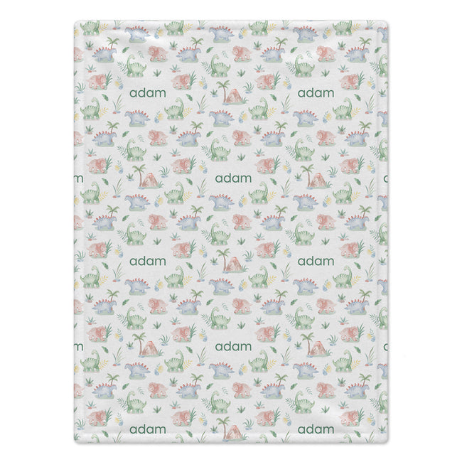 Baby Dinosaurs blanket personalized with Adam, featuring pastel green, blue, and peach dinosaurs, plants, eggs, and volcanoes.