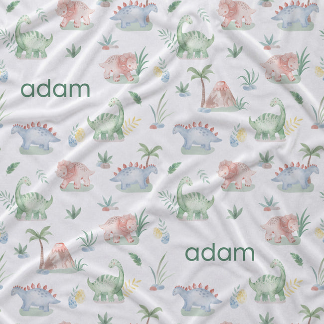 Personalized baby fabric featuring a colorful dinosaur pattern on a white background with the name 'adam' printed in green text.