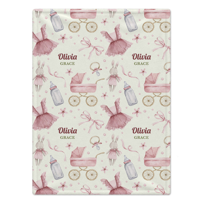 A personalized baby blanket with a repeating pattern of pink prams, bottles, bunnies, and bows on a cream background, featuring the custom text 'Olivia GRACE' in the center.