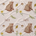 Personalized fabric print featuring a repeating pattern of brown watercolor bears, yellow flowers, mushrooms, and green leaves on a cream background, with the name 'OWEN' printed in brown text.