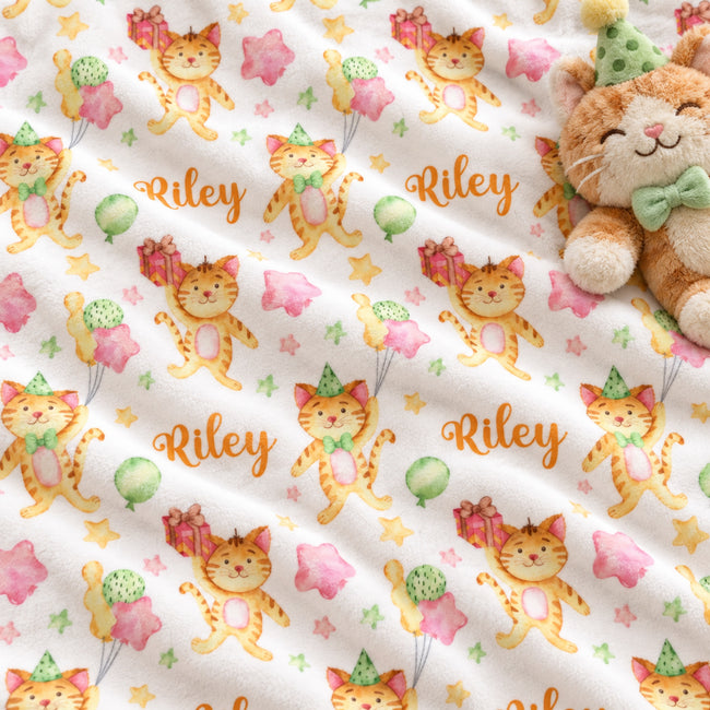 A close-up of a white fabric with a repeating print of orange cartoon cats wearing party hats, pink stars, green balloons, and the name Riley in orange script. A plush teddy bear with a green bow tie is partially visible on the right side.
