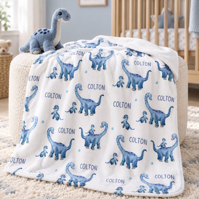 Personalized dinosaur baby boy blanket featuring blue dinosaurs and a custom name on a white background.
