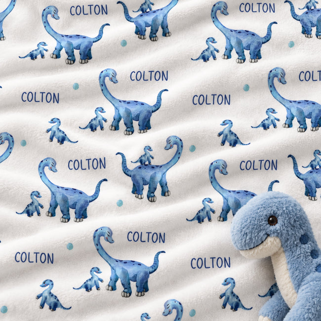 Personalized dinosaur baby boy blanket featuring blue dinosaurs and a custom name on a white background.