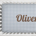 A fitted crib mattress with a light blue and white gingham check pattern and the name 'Oliver' printed in brown script across the right side, shown inside a white wooden crib.