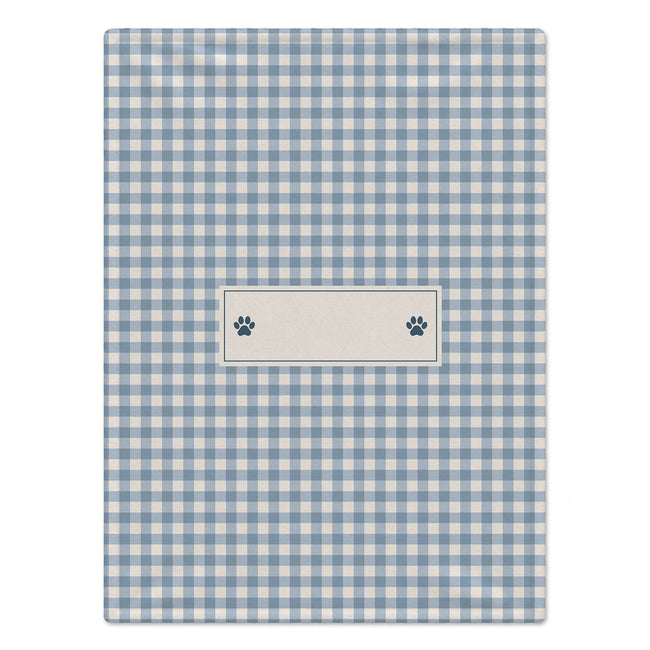 A rectangular blue and white gingham checkered dog blanket with a central cream label area featuring two small dark paw prints, shown on a plain white background.