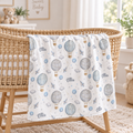 A personalized baby blanket with a hot air balloon pattern draped over a wicker bassinet in a bright nursery setting.