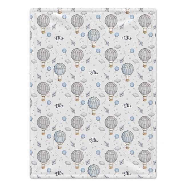 A rectangular baby blanket with a repeating pattern of hot air balloons, paper airplanes, and the name 'Ellie' in script, shown flat against a white background.