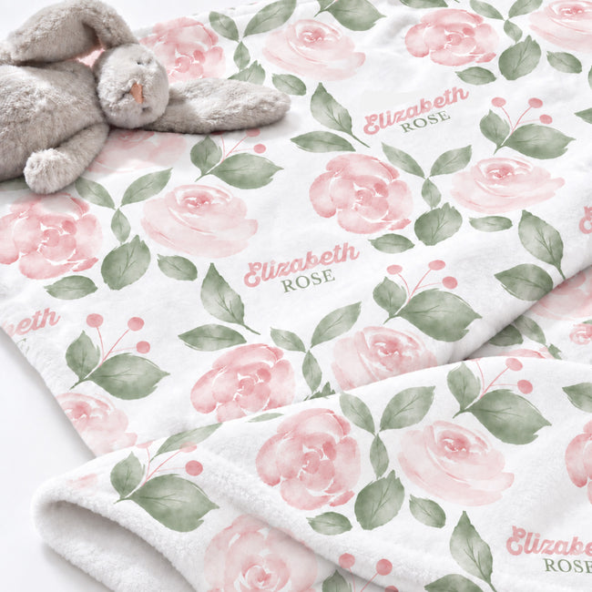 Close-up of Blush Rose Garden baby blanket with pink roses, sage leaves, and Elizabeth Rose lettering beside a plush bunny.