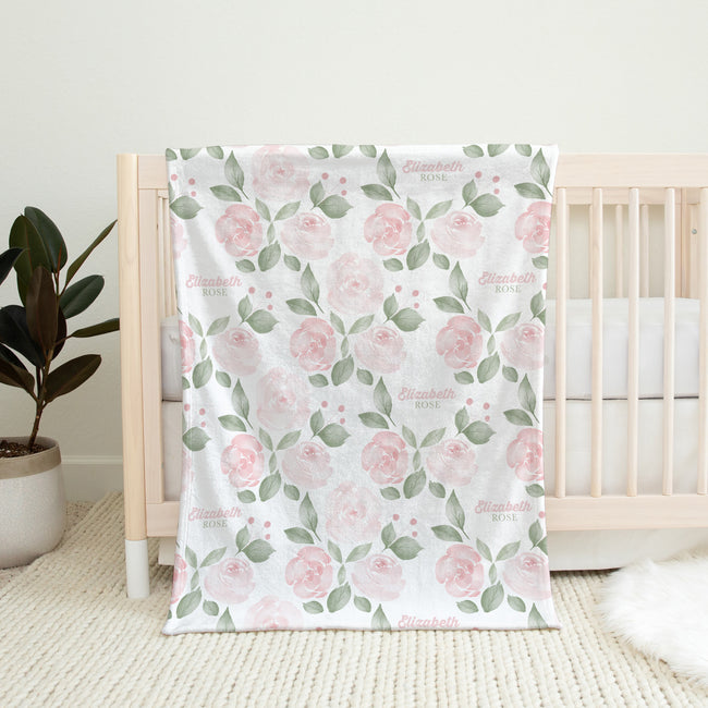 Blush Rose Garden personalized baby blanket with pink roses and sage leaves, draped over a natural wood crib.