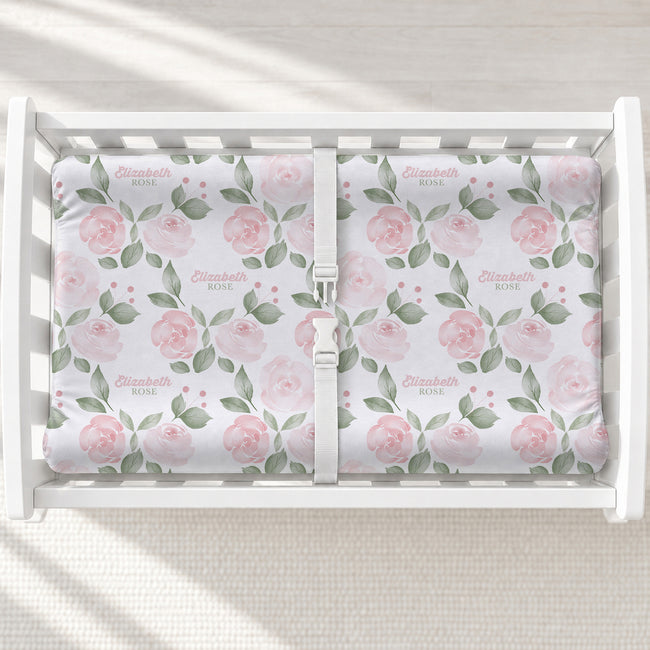 Blush Rose Garden changing pad cover with pink roses, sage leaves, and the name Elizabeth Rose, shown on a white changing table.