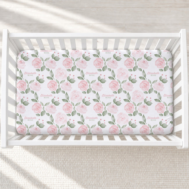 Overhead view of Blush Rose Garden personalized crib sheet with pink roses, sage leaves, and the name Elizabeth Rose in a white crib.