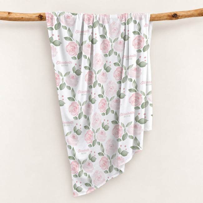 Blush Rose Garden swaddle personalized with Elizabeth Rose, featuring pink roses and sage leaves, draped over a wooden branch.