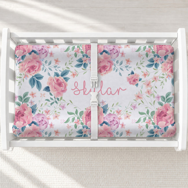 A white changing table with a personalized changing pad cover featuring a floral-patterned mattress protector with pink roses, green leaves, and the name 'Skylar' in pink script. 
