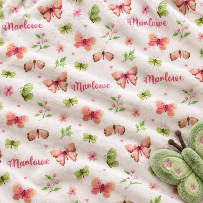 Personalized Butterfly and Flower Baby Girl Blanket. Pink, peach, and green butterflies flutter among flowers, leafy sprigs, and tiny hearts around a custom name.