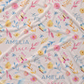 A close-up of a fabric surface with a repeating watercolor floral and butterfly print on a warm off-white background. The pattern includes pink and yellow flowers, blue and yellow leaves, and pink and blue butterflies.