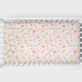 A crib mattress fitted sheet with a pastel watercolor floral pattern and the personalized text 'AMELIA grace' printed repeatedly, shown inside a white wooden crib.