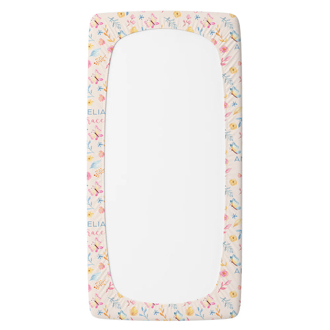 A personalized twin fitted sheet featuring a delicate pastel floral border pattern in pink, yellow, blue, and green on a light cream background.