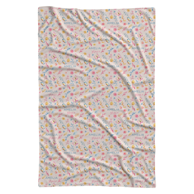 A rectangular swaddle blanket with a delicate, all-over repeating pattern of small birds, flowers, and the name 'AMELIA' printed in blue. The blanket is laid flat against a solid white background.