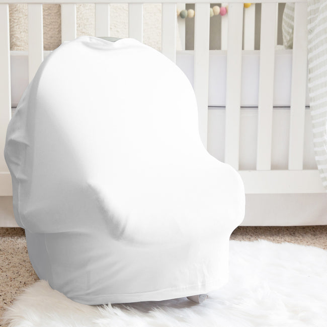 A white baby car seat cover fitted over a car seat, placed in a nursery setting in front of a white crib on a white faux fur rug.
