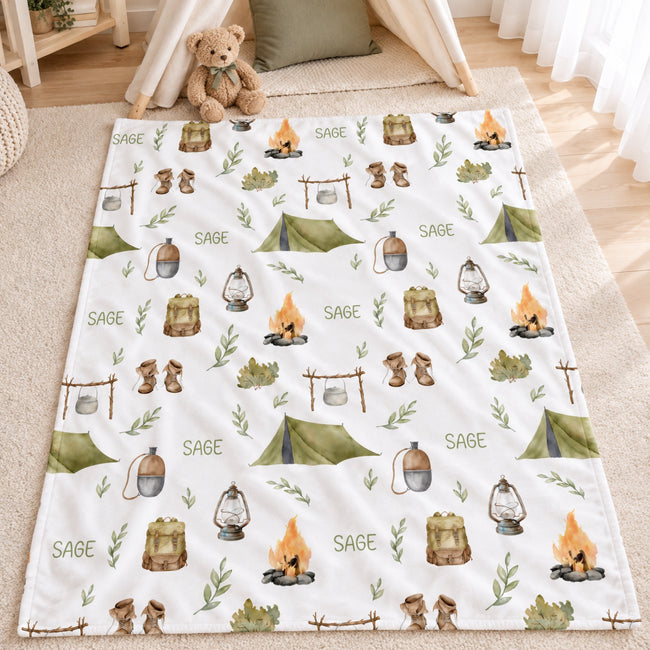 Personalized Camping Baby Blanket. Tents, campfires, lanterns, and outdoor adventure details surround a custom name in earthy woodland colors.