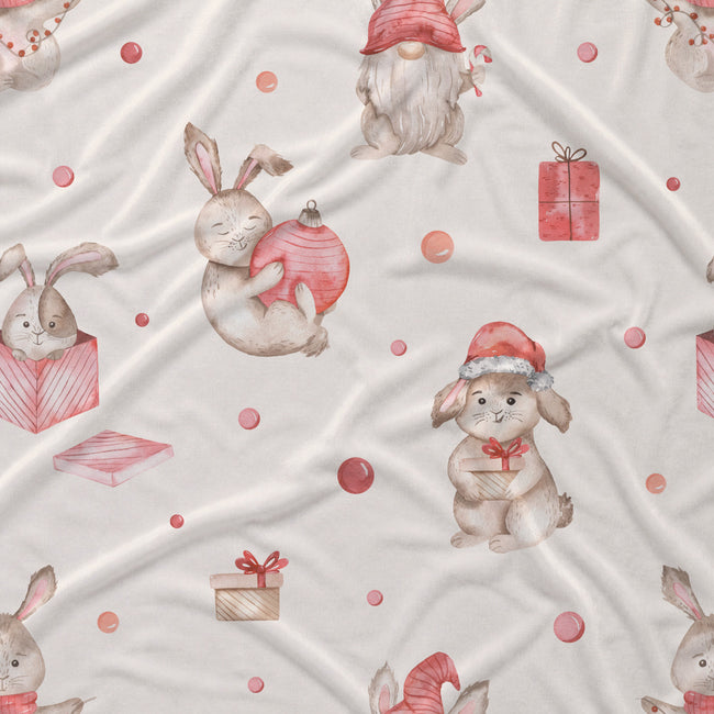 A close-up of a light cream fabric with a repeating watercolor pattern of rabbits, gnomes, and wrapped gifts in soft pink, red, and beige tones.