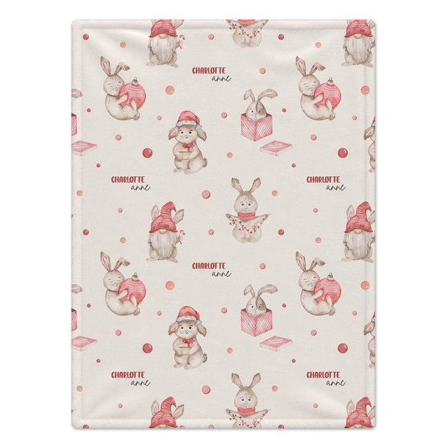 A blanket featuring a repeating pattern of cute cartoon rabbits wearing red Santa hats and holding pink hearts, with the name 'Charlotte' printed in red text.