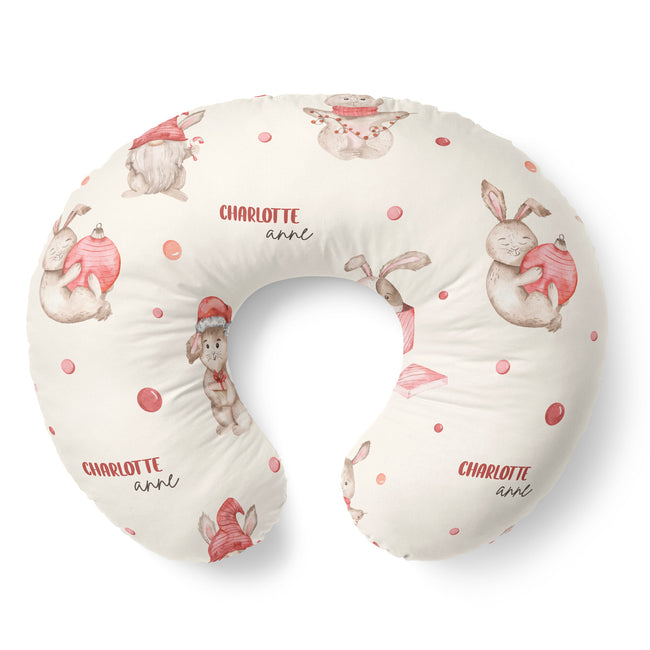 A U-shaped baby nursing pillow with a cream background, decorated with watercolor-style bunnies in red and pink, and the personalized name 'CHARLOTTE annl' printed in red and black.