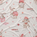 A close-up of a light cream fabric with a printed pattern of Easter bunnies, gnomes, and pink gift boxes, with the text 'CHARLOTTE annl' printed in red and black.