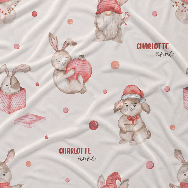 A close-up of a light cream fabric with a printed pattern of Easter bunnies, gnomes, and pink gift boxes, with the text 'CHARLOTTE annl' printed in red and black.