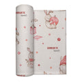 A personalized swaddle blanket featuring a watercolor-style pattern of Easter bunnies, gnomes, and pink holiday ornaments on a warm cream background.