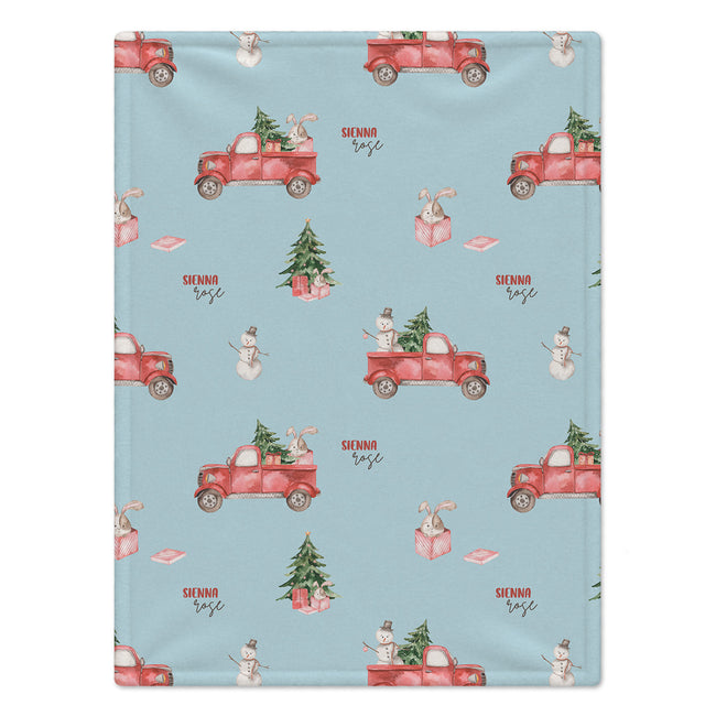 A personalized blanket featuring a light blue background with a repeating Christmas-themed pattern of red pickup trucks, snowmen, snow globes, and Christmas trees. 