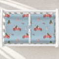 A white changing table with a personalized changing pad cover featuring light blue background and a festive Christmas theme, featuring red pickup trucks carrying Christmas trees and gifts, snowmen, and small trees. 