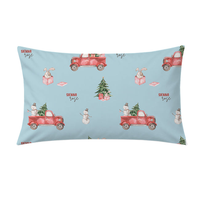A rectangular light blue pillow sham featuring a repeating Christmas-themed pattern with red vintage pickup trucks carrying Christmas trees, snowmen, gift boxes, and the text 'SIFNNO ROSE'.