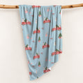 Personalized Christmas swaddle blanket hanging on a wooden rail with red vintage trucks, Christmas trees, snowmen, bunnies and custom name.