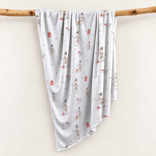 Personalized Christmas swaddle blanket hanging on a wooden rail with watercolor snowmen, red vintage trucks, Christmas trees and custom baby name.