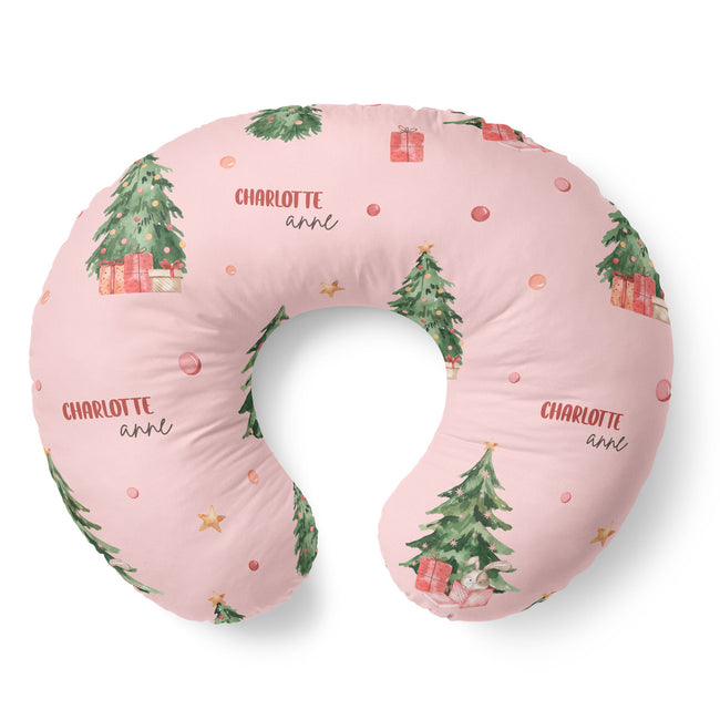 A U-shaped nursing pillow in light pink with a watercolor Christmas tree and gift print, featuring the personalized name 'CHARLOTTE ann' in red and black script.
