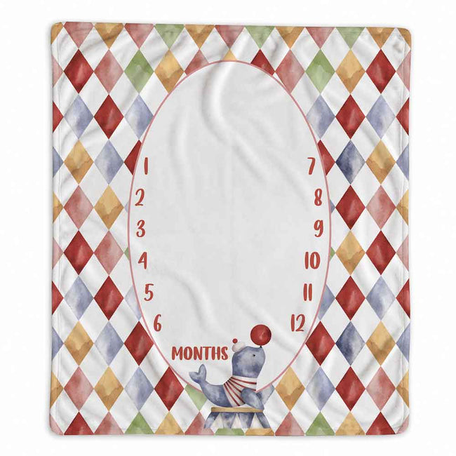 A square baby milestone blanket with a colorful harlequin diamond border and a large white oval center for writing months, decorated with a small juggling elephant at the bottom.