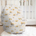 A baby car seat cover with a construction-themed print featuring yellow excavators, blue cranes, and the name 'MASON' on a light gray background, styled in a nursery setting in front of a white crib.