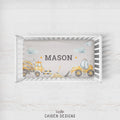 A baby crib bedding set featuring a personalized nursery print with construction vehicles and the name 'MASON' in the center, displayed in a white wooden crib on a light wood background. The brand 'CAIDEN DESIGNS' is visible at the bottom.